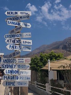 a pole with many signs on it in front of a building and some mountains behind it