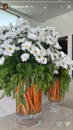 some carrots and daisies in a glass vase on a counter with white flowers