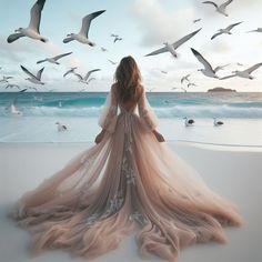 a woman is standing on the beach with birds flying around her and she's looking at the ocean