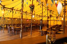 the inside of a large tent with tables, chairs and lamps on it's sides