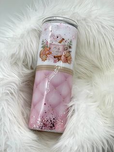 a pink tumbler cup sitting on top of a white fur covered floor next to a teddy bear