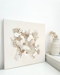 a white wall with flowers on it next to a vase filled with flowers and two stacks of books