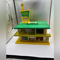 a doll house with a green roof and yellow trim on the top shelf is sitting in front of a washing machine