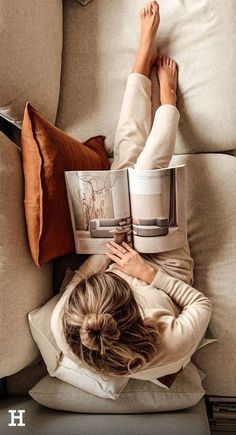 a woman laying on top of a couch reading a book