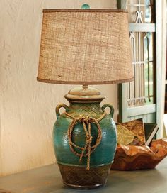 a green vase sitting on top of a table next to a lamp with a brown shade