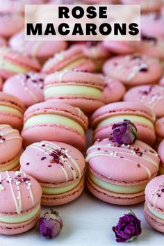 many pink macaroons with white frosting and purple flowers on them are laying next to each other