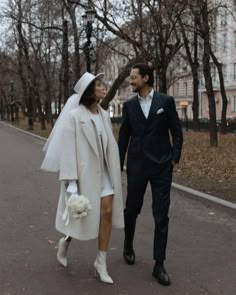 a man and woman dressed in white walking down the street with their hands behind each other