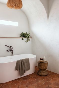 a white bath tub sitting under a window next to a plant in a potted planter