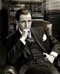 a black and white photo of a man sitting in a chair with his hand on his chin