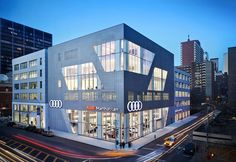 an audi dealership with cars parked in front of it at dusk, lit up by street lights