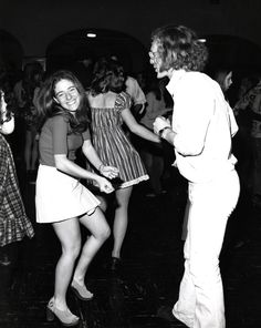 black and white photograph of two women dancing at a party with other people in the background