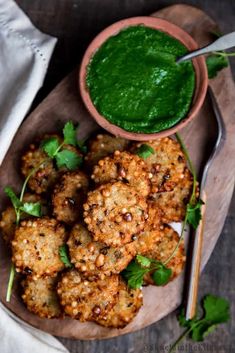 some food is sitting on a wooden plate with a green sauce in the bowl next to it