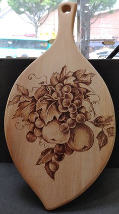 a wooden cutting board with an image of grapes and apples painted on it's side