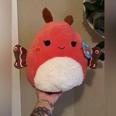 a hand holding a red stuffed animal with white and brown wings on it's face