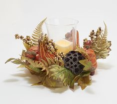 a candle and some leaves on a white table top with a glass in the middle