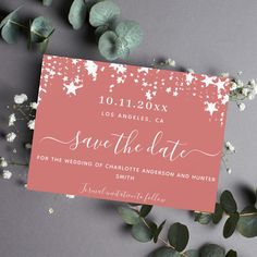 wedding save the date card with pink and white stars on it, surrounded by greenery