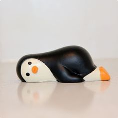 a small black and white penguin with an orange beak sitting on the floor next to a wall