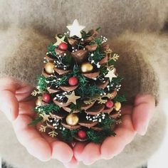 a small christmas tree made out of pine cones in someone's hands with ornaments on it