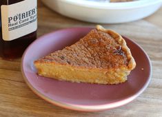 a piece of pie on a pink plate next to a bottle of beer and bowl