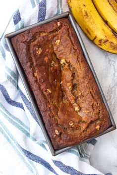 a loaf of banana bread sitting on top of a blue and white towel next to two bananas