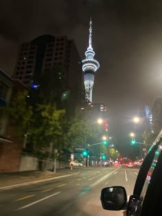 a car driving down a street at night with the sky tower in the back ground