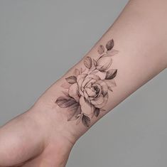 a woman's arm with a rose tattoo on it and leaves around the wrist