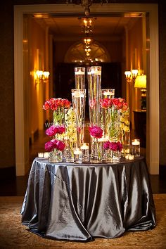 a table topped with lots of vases filled with pink and red flowers next to candles