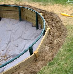 a dog is laying in the sand inside an empty wooden pit with green fencing around it