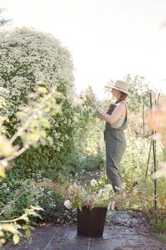 a woman in overalls and a hat standing next to a bush