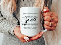 a woman holding a white coffee mug with the words jesus printed on it, in her hands