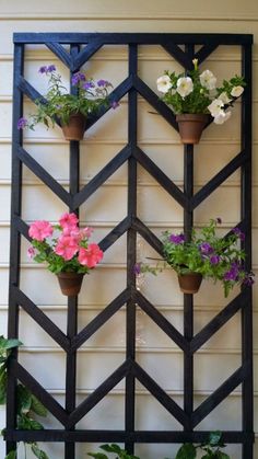 an iron trellis with potted flowers hanging on it's sides and attached to the wall