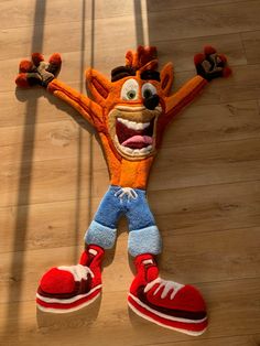 an orange stuffed animal laying on top of a wooden floor next to a pair of red shoes