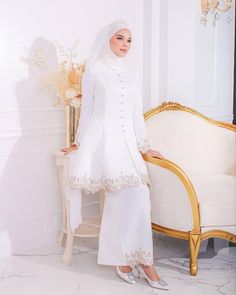 a woman in a white outfit standing next to a gold chair and table with flowers on it