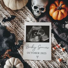 a baby announcement is displayed on a table with halloween decorations and skeleton heads in the background