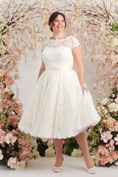 a woman standing in front of a floral arch wearing a white dress and high heels