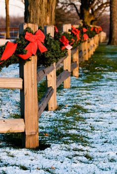 a row of wooden fence with wreaths and bows on it's posts in the snow