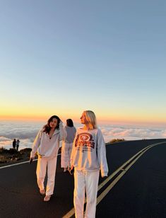 two women walking down the road with clouds in the background and one woman wearing white