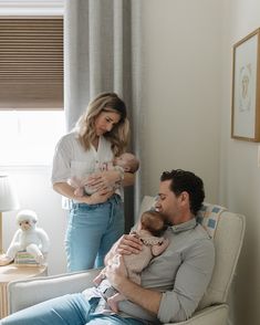 a man holding a baby while sitting in a chair next to a woman and child