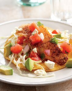 a white plate topped with chicken and veggies on top of rice next to an avocado wedge