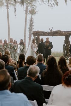 a couple getting married in front of an outdoor wedding ceremony with palm trees and fog