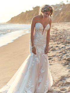 a woman standing on top of a beach next to the ocean wearing a wedding dress