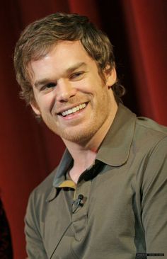 a man smiling while sitting in front of a red curtain