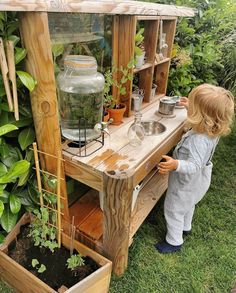 a little boy standing next to a wooden planter filled with plants and water in it