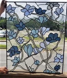 a person is holding up a stained glass window with blue flowers on it and palm trees in the background