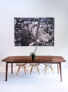 a wooden table with two chairs and a vase on it in front of a cityscape