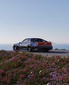 a black car driving down a road next to purple flowers