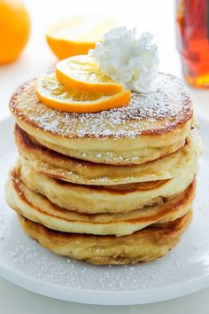 a stack of pancakes topped with powdered sugar and orange slices