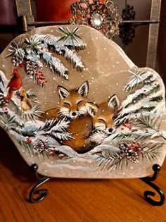 a glass plate with two foxes and pine cones on it sitting on a wooden table