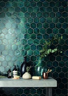 a shelf with vases and other items on top of it in front of a green tiled wall