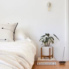 a bed with white sheets and pillows next to a potted plant on top of a book